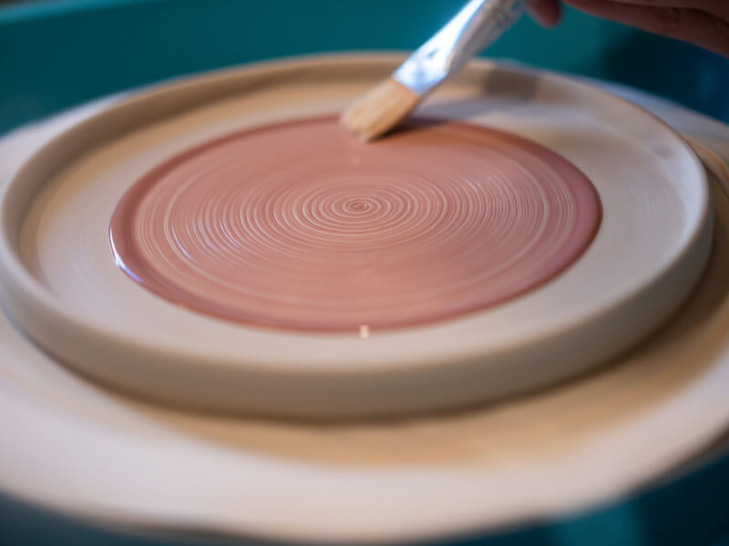 A person paints a plate red at a ceramic painting class.
